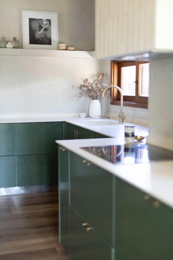 Modern kitchen interior with green cabinets, white countertops, and natural light.