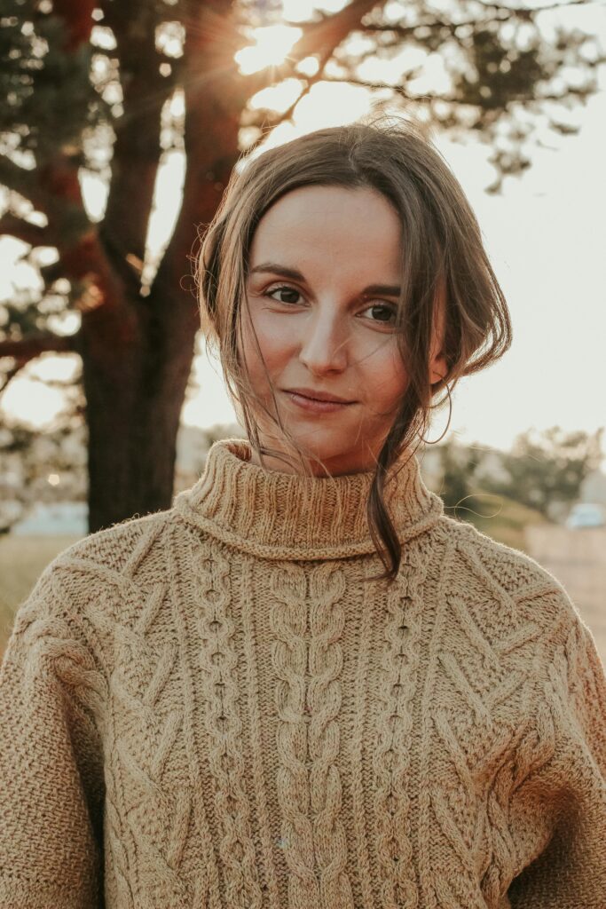Charming portrait of a woman wearing a knitted sweater outdoors with warm sunlight creating a cozy atmosphere.